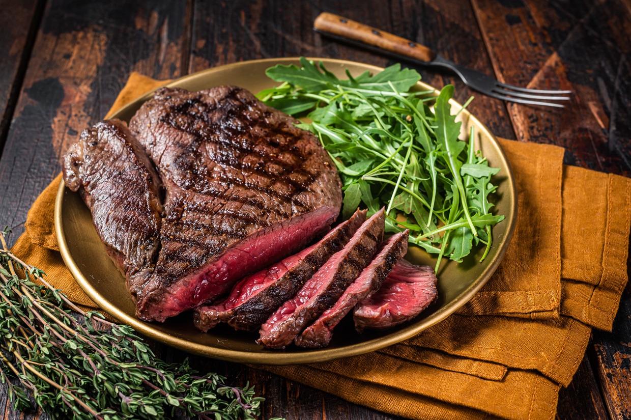 BBQ dinner with top sirloin beef steak and salad on a plate. Wooden background. Top view.